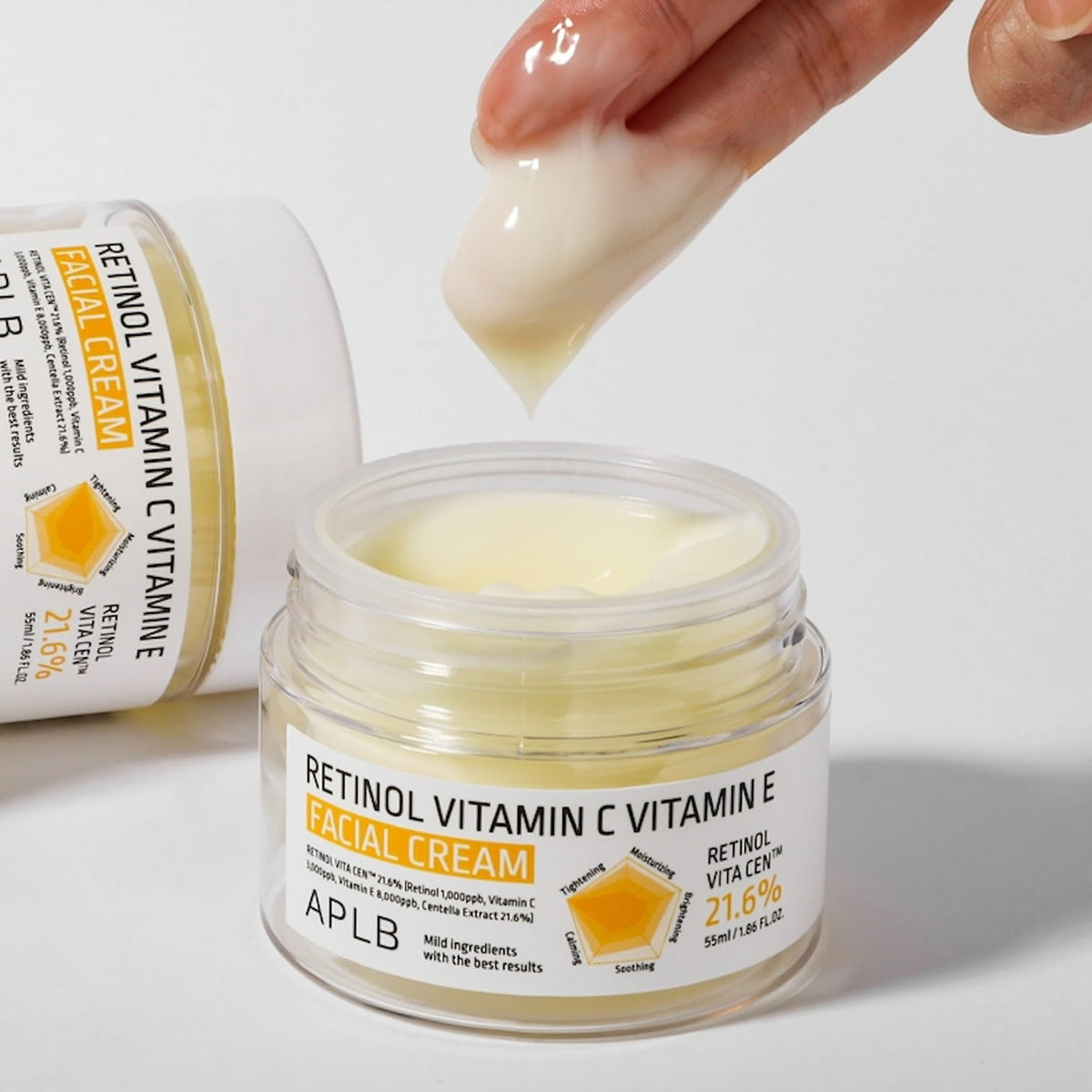 Hand applying APLB Retinol Vitamin C Vitamin E Facial Cream from a jar with visible branding on a light grey background