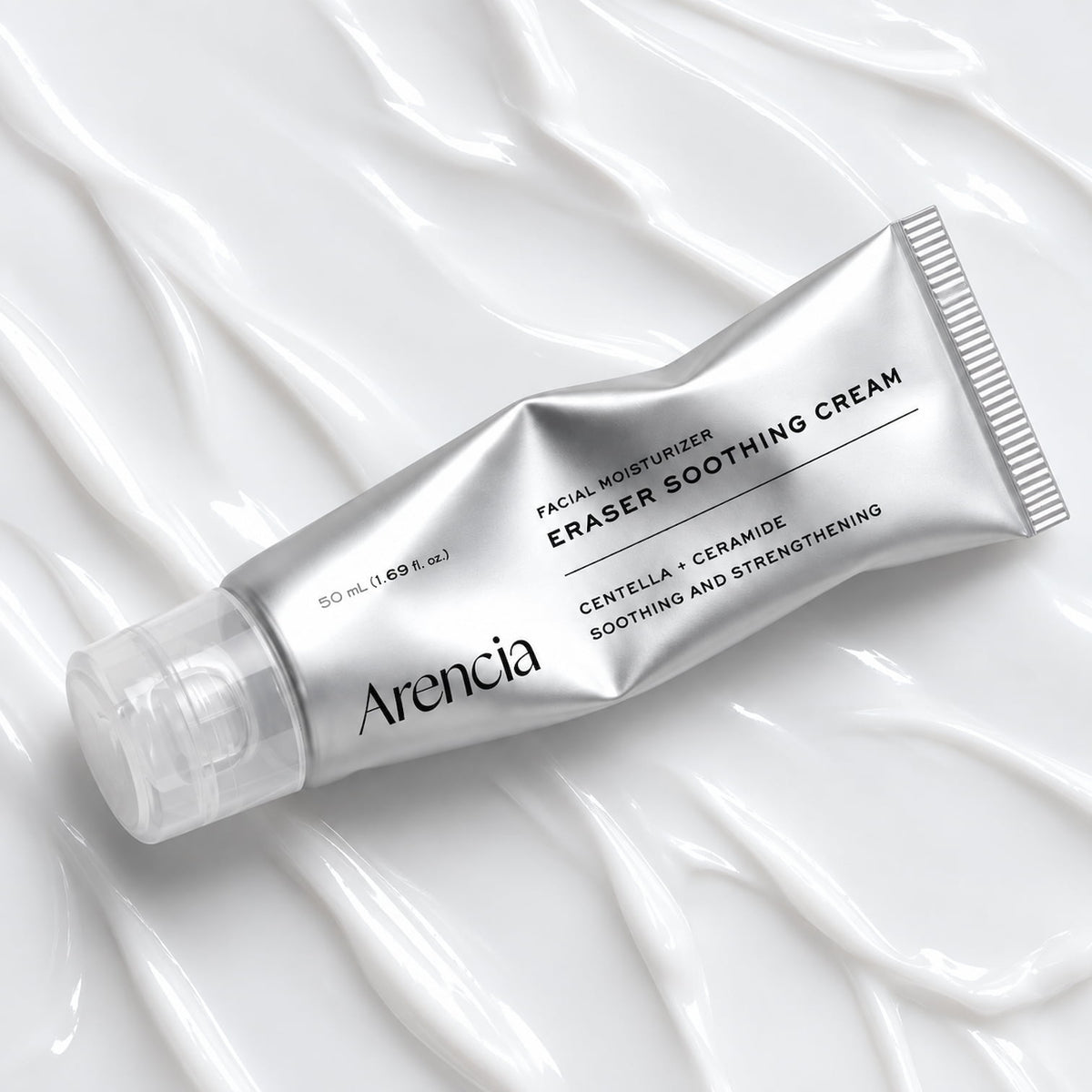 A silver squeeze tube of Arencia Facial Moisturizer Eraser Soothing Cream, placed diagonally on a background of white cream swirls.
