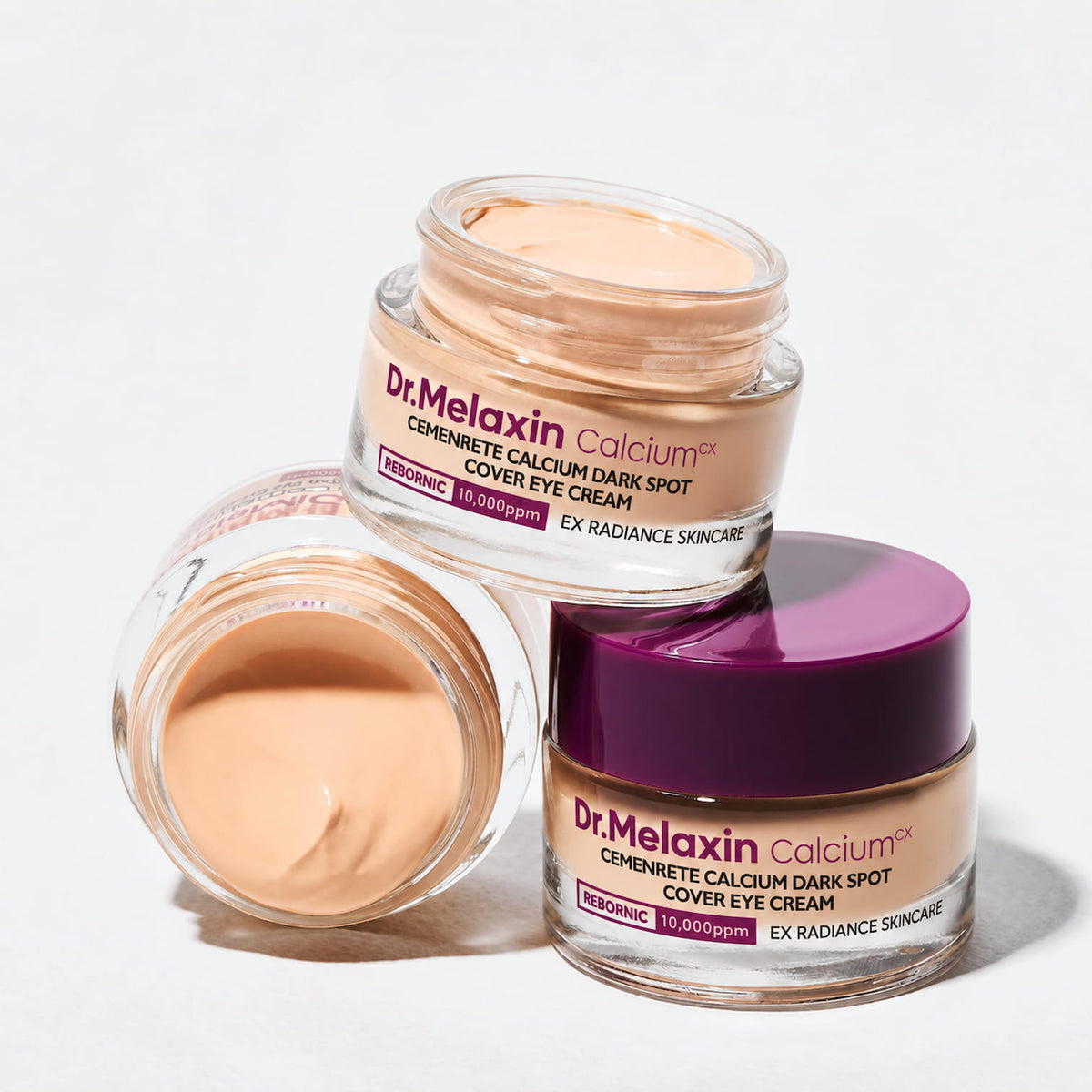 Three jars of Dr. Melaxin Cemenrete Calcium Dark Spot Cover Eye Cream arranged on a clean white background, showing both the open cream and the closed jar with its purple lid.