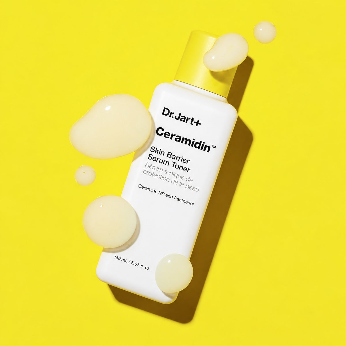 A bottle of Dr. Jart+ Ceramidin Skin Barrier Serum Toner with a yellow cap, shown on a bright yellow background with decorative serum droplets.