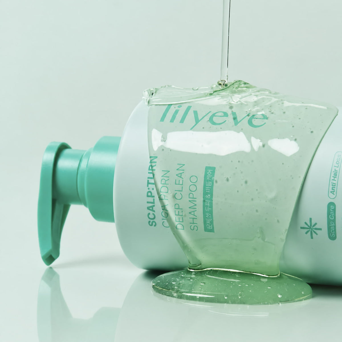 A bottle ofLILYEVE Scalp Turn Cica PDRN Deep Clean Shampoo lying on its side with a clear gel-like product dripping from above and pooling at the base, on a light turqoise background.
