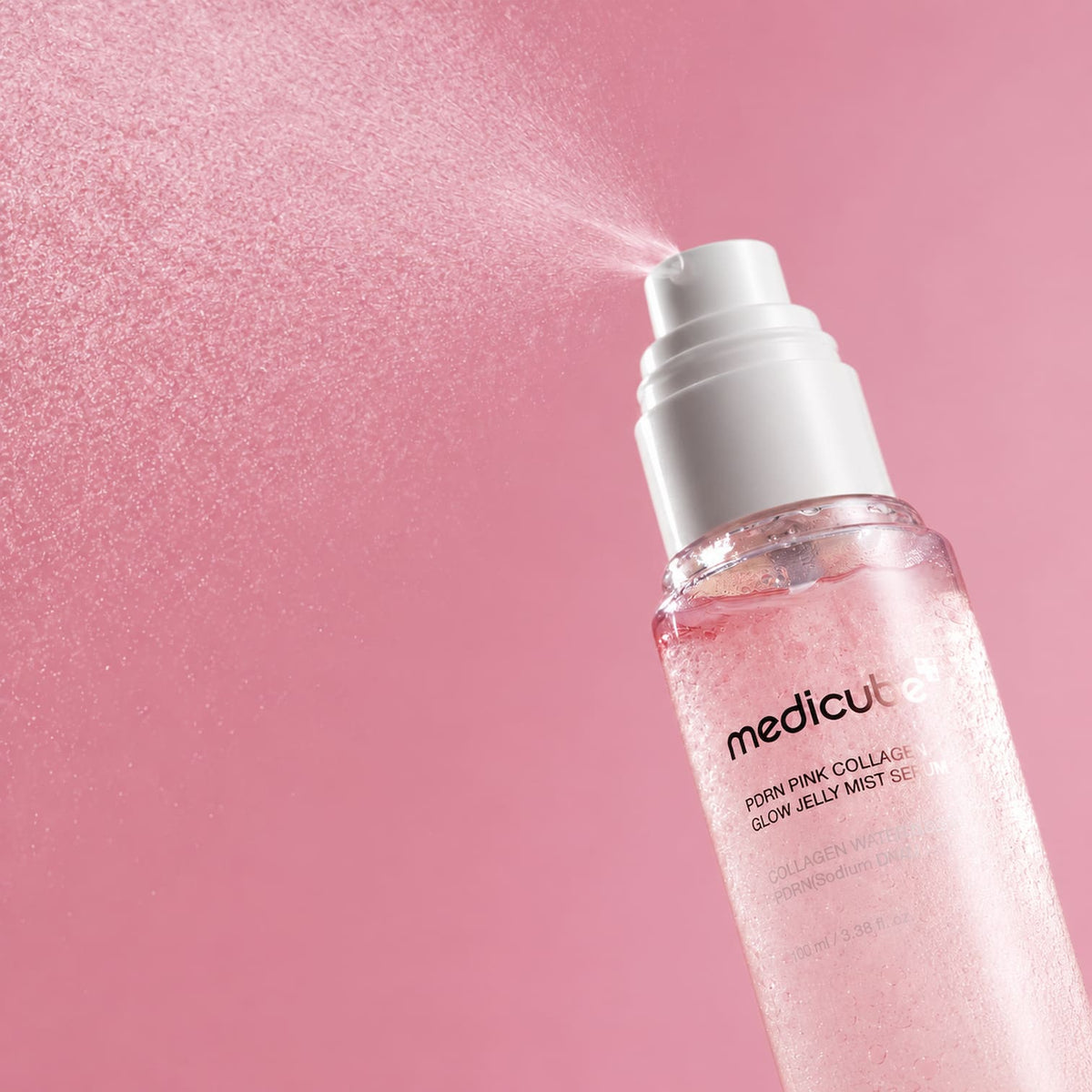 MEDICUBE PDRN Pink Collagen Glow Jelly Mist Serum spray bottle with a white pump, shown spraying pink mist against a solid pink background.