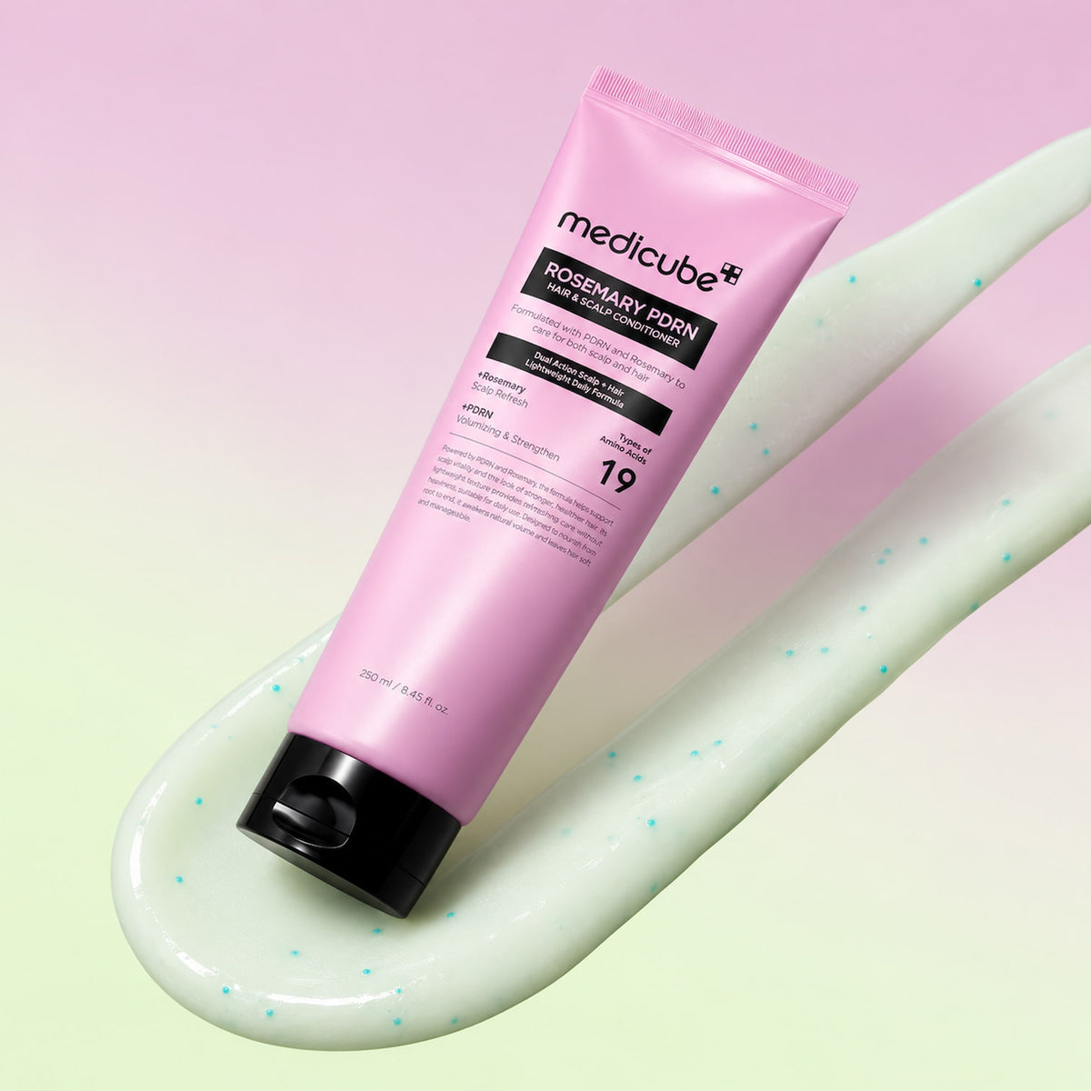A pink tube of MEDICUBE Rosemary PDRN Hair & Scalp Conditioner with a black cap, resting diagonally on a light green gel smear against a pink and green gradient background.