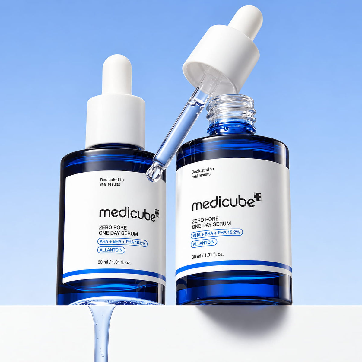 Two blue glass dropper bottles of medicube Zero Pore One Day Serum on a white surface against a light blue gradient background. One bottle has its dropper cap off and the glass dropper is shown above it, with serum dripping from the bottle.