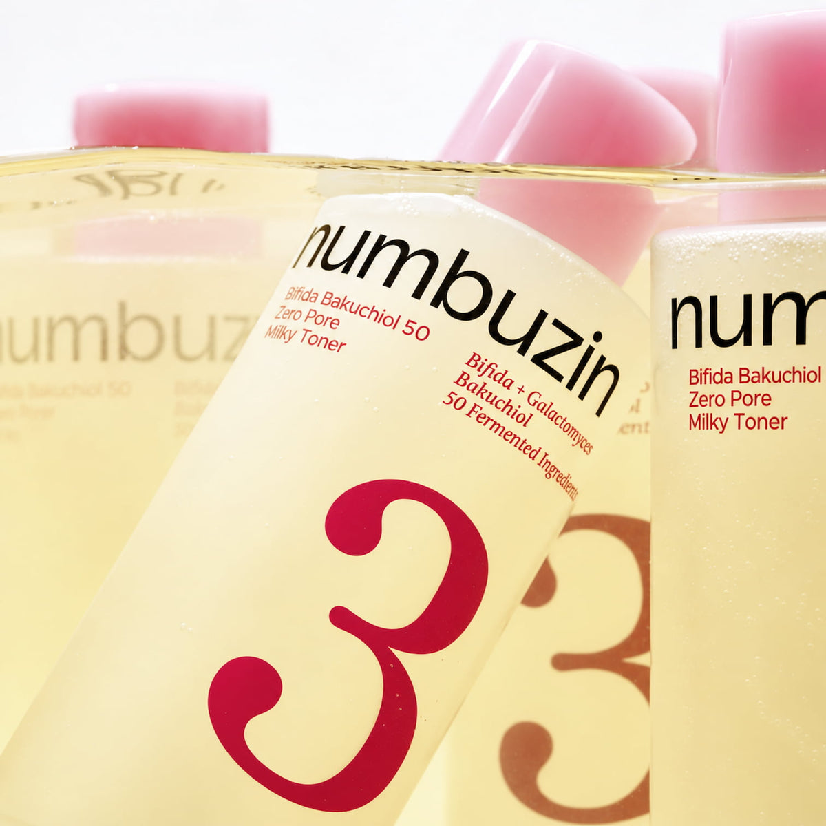 Three close-up views of a NUMBUZIN No.3 Bifida Bakuchiol 50 Zero Pore Milky Toner bottle, showing the pale yellow liquid, pink cap, and white label with red text and a large red number 3.