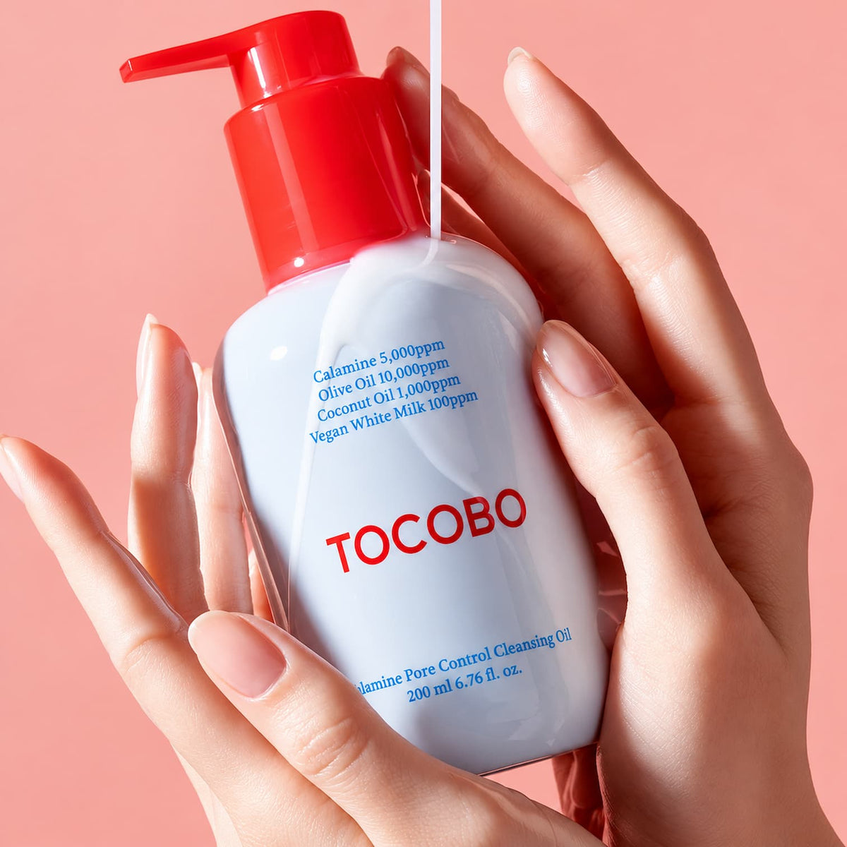 A hand holds a white bottle of TOCOBO Calamine Pore Control Cleansing Oil with a red pump dispenser against a solid pink background.