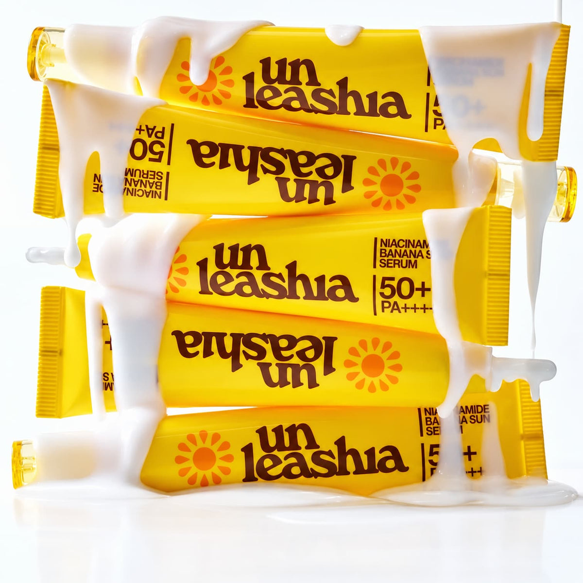 Four yellow tubes of UNLEASHIA Niacinamide Banana Sun Serum SPF 50+ arranged in a stack with white liquid dripping from the top, on a white background.