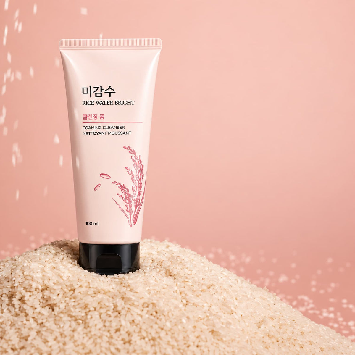 A 100 ml squeeze tube of Rice Water Bright Foaming Cleanser standing upright in a mound of uncooked rice against a soft pink background.